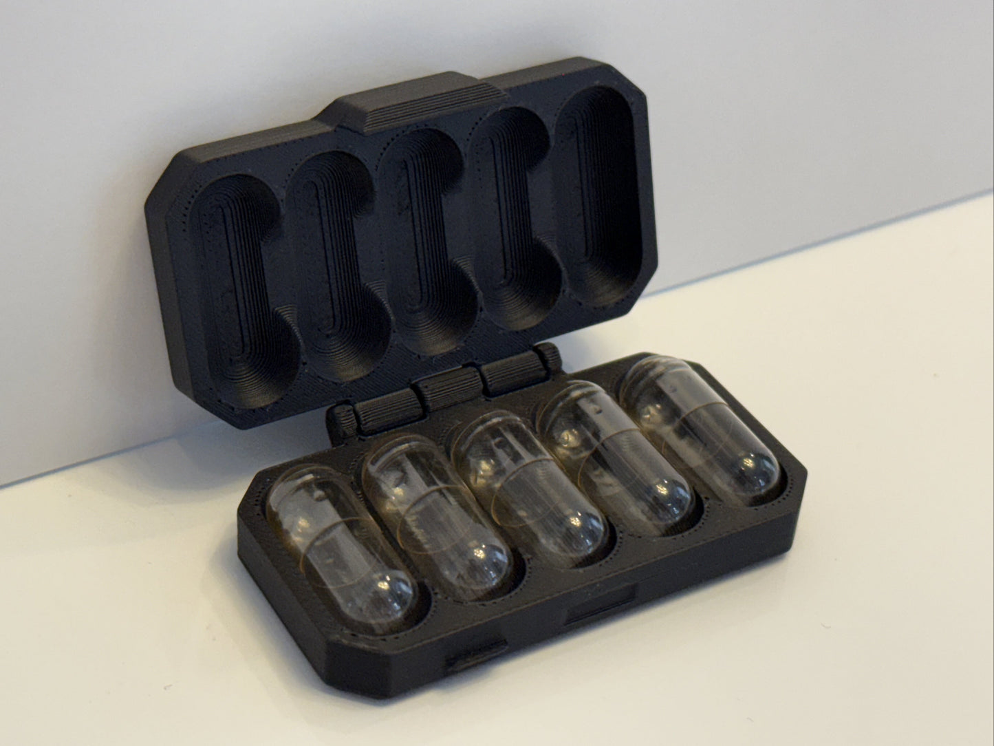 Black case with five clear cylindrical containers on a light gray surface.