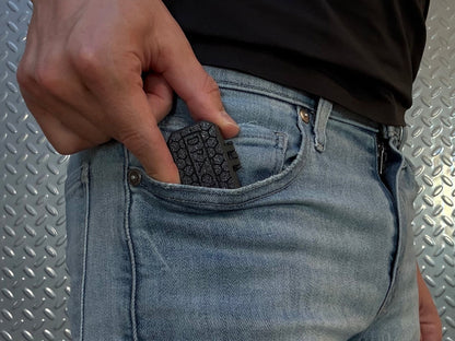 Person wearing light blue jeans with a black shirt, standing in a room with a metallic wall with Dpack in their pocket.